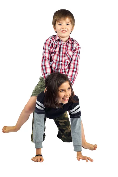 A young girl gives her little brother a horseback ride on a white background.  They are isolated with a clipping path.  Both kids are wearing camouflage pants.