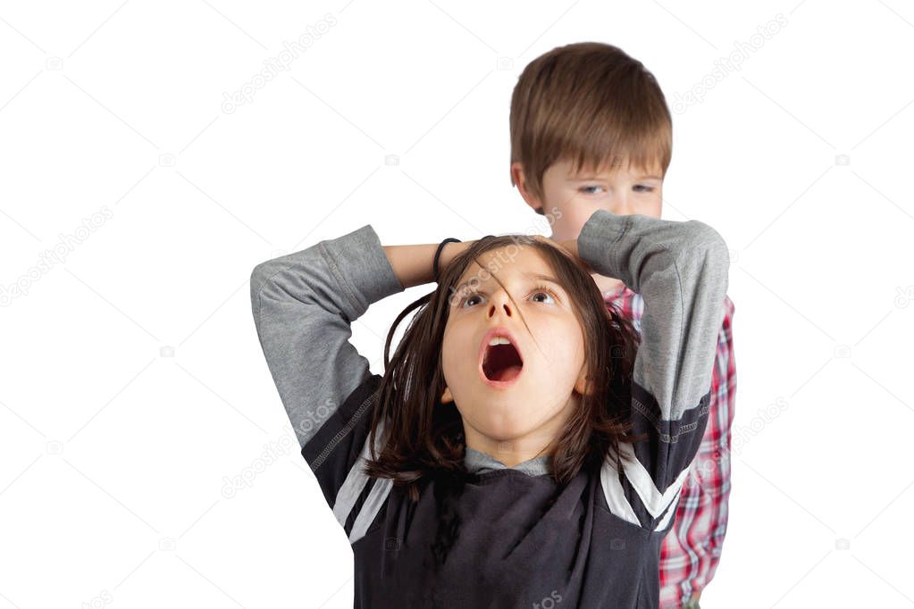 A little brother pulls the hair of his older sister.  He looks sly and mischievous.  She grabs her head with an open mouth look of shock and pain.