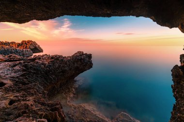 Paralimni, Kıbrıs'ta gün batımında Cape Greco kayalıkları ve kayaların inanılmaz gün batımı görüntüsü. Turkuaz mavisi denizi ile renkli kırmızı, pembe ve sarı gökyüzü. 