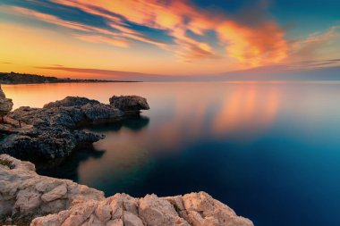 Amazing sunset image of Cape Greco cliffs and rocks on a sunset in Paralimni, Cyprus. Colorful red, pink and yellow skies with turquoise blue sea.  clipart