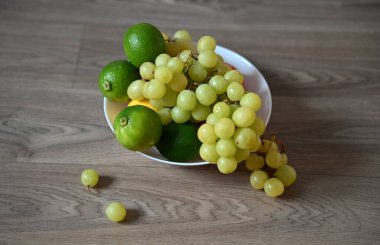 Ahşap bir yüzeyde beyaz bir kase yeşil üzüm ve limon karışımı ile dolup taşıyor. Bazı üzüm çeşitleri dağılır, dinamik, doğal ve sağlıklı bir yaşam formu oluşturur..