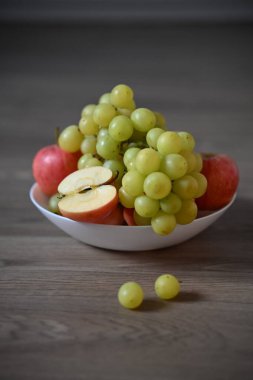 Yeşil üzümler ve kırmızı elmalardan oluşan taze bir karışım. Çekirdeğini göstermek için dilimlenmiş bir elma. Tahta bir masada beyaz bir kasede. Kompozisyon parlak ve doğal..