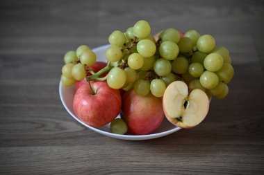 Yeşil üzümler ve kırmızı elmalardan oluşan taze bir karışım. Çekirdeğini göstermek için dilimlenmiş bir elma. Tahta bir masada beyaz bir kasede. Kompozisyon parlak ve doğal..