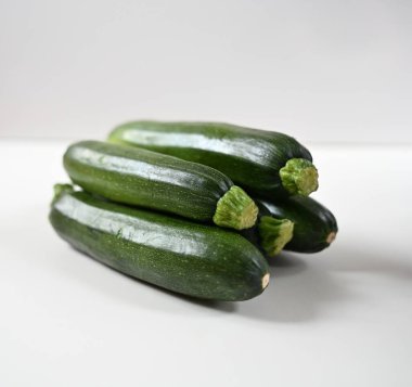 Küçük, koyu yeşil bir kabak yığını, sapları görünür, beyaz bir arka plan üzerine çekilmiş. Görüntü basit, temiz ve sağlıklı malzemeleri sergilemek için mükemmel..