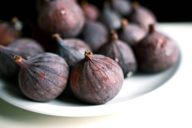 Temiz beyaz bir tabakta bütün ve dilimlenmiş incirlerin iştah açıcı yakın çekimi. Üst düzey yemek blogları, gurme tarifleri, pişirme ve sağlıklı tatlı promosyonları için ideal..