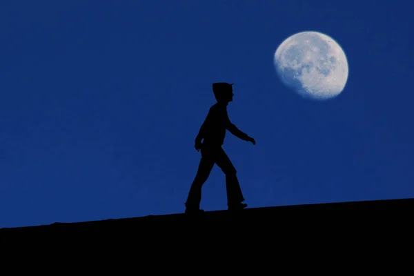 Silhouette of a person walks up a hill with the sky in the background