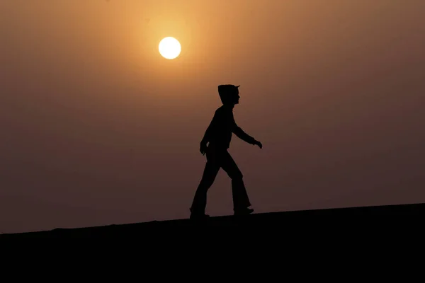 Silhouette of a person walks up a hill with the sky in the background