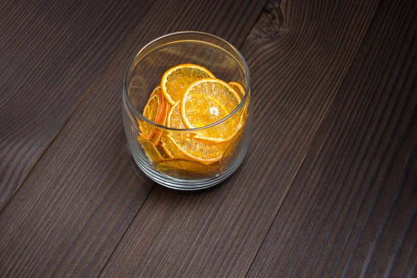 Fruit chips. Bright dried slices of orange in a glass jar on a dark wooden background.