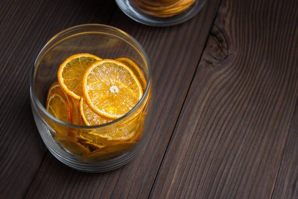 Fruit chips. Bright dried slices of orange in a glass jar on a dark wooden background. Place for text on the right