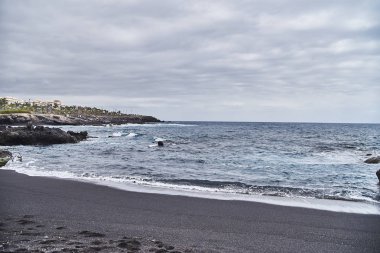 Siyah kum ile olağandışı plaj. Güzel temiz plaj sıcak deniz, okyanus. Güneşlenmek için zamanı. Boş tesisi alanı. Volkanik kayalar suya yakın. Dalgalar sıçrama sahile hakkında.