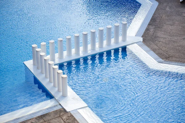 A beautiful and unusual pool in an expensive resort. White decorative bars. Crystal clear blue water in a swimming pool. Top view of the hotel's outdoor swimming pool. Time of relaxation.