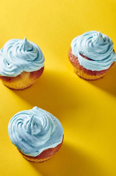 Unusual cupcakes with a beautiful blue cream. Cakes with perfect caps made from protein cream. Whipped cream with blue food color. Treat for children on a yellow-blue background.