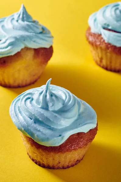 Unusual cupcakes with a beautiful blue cream. Cakes with perfect caps made from protein cream. Whipped cream with blue food color. Treat for children on a yellow-blue background.