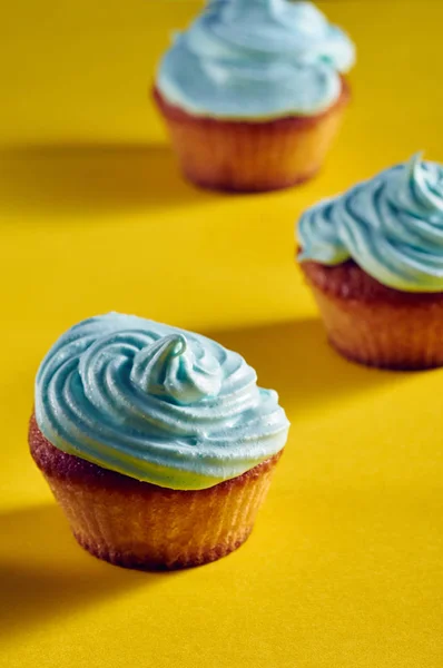 Unusual cupcakes with a beautiful blue cream. Cakes with perfect caps made from protein cream. Whipped cream with blue food color. Treat for children on a yellow-blue background.
