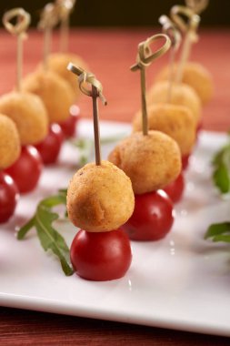 Festival tablo için iştah açıcı ve sıradışı snack. Bir şiş üzerinde küçük bir ikram. Küçük yuvarlak pirzola ekmek kırıntıları ve kiraz domates. Vejetaryen yemek patates top ve domates ile.