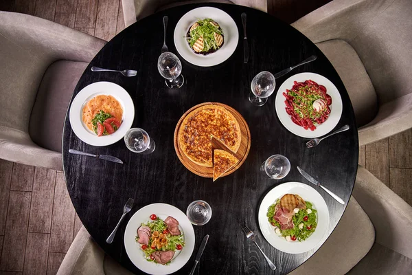 Chic black table with a variety of delicious dishes from the chef in a cafe, restaurant. The dining table is ready and reserved for guests. Cheese cake in the center of the table.