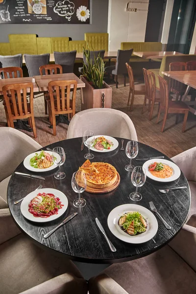 Cozy family restaurant, cafeteria, cafe, bar. The festive table is served with an abundance of dishes and awaits guests, customers, visitors, a big company. Five gourmet dishes and pizza in the center
