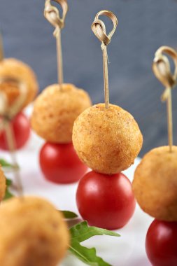 Festival tablo için iştah açıcı ve sıradışı snack. Bir şiş üzerinde küçük bir ikram. Küçük yuvarlak pirzola ekmek kırıntıları ve kiraz domates. Vejetaryen yemek patates top ve domates ile.