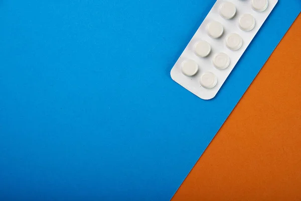 A pack of plain white pills on a two-tone blue-orange background. Drugs in the pharmaceutical packaging. Illegal distribution of narcotic drugs from drug trafficker. Drug therapy from a therapist.