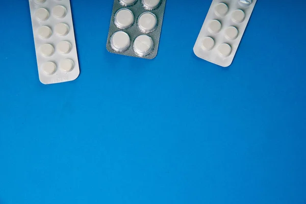 Two kinds of simple white pills from the pharmacy on a bright blue background table. Minimalistic advertising of drugs, pharmacies. Medicines for various diseases.