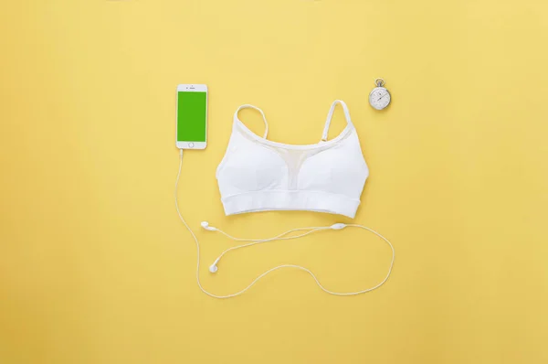 Sport time. Sports flat lay on yellow background. White sports topic, mobile phone with headphones, vintage stopwatch in vintage style. Green screen on the smartphone for your text.