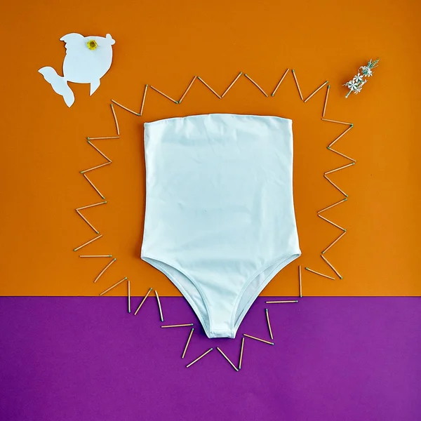Beautiful unusual outfit presentation for fashion blog, advertising, clothing catalog. Trendy white strapless swimsuit. Unusual decor of matches and paper fish. White bikini on a bright background.