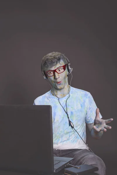 年轻有趣的家伙 在眼镜和耳机的多彩多姿的油漆击中 正在谈论起劲通过计算机 — 图库照片