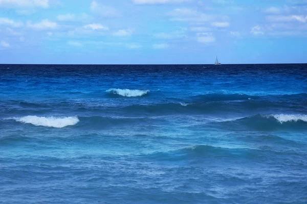 Waves of the blue ocean with a blue sky, on the horizon a sailboat, background