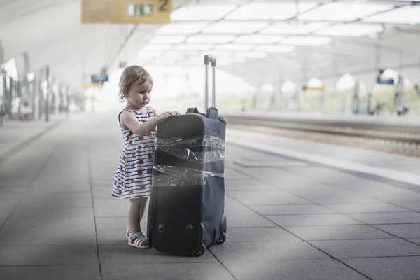 little sweet girl with a large travel suitcase on a deserted railway perforator