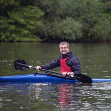 Spor kayık kayık geniş bir nehir üzerinde gülümseyen genç atletik erkek oturuyor