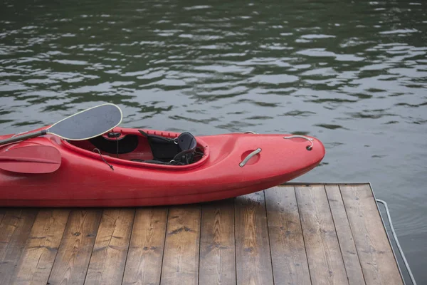 red kayak sport boat rests on a wooden dock on the shore