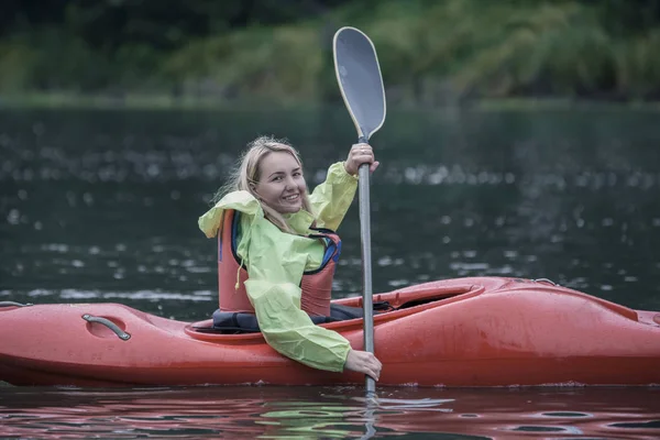 Young blonde girl swims on a sports boat kayak on a beautiful river