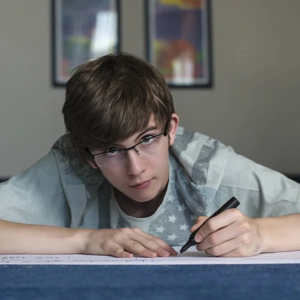 戴眼镜的青少年学生躺在地板上 然后在纸上写一支毡尖笔 — 图库照片