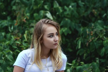 Yeşil bitki örtüsü bir arka plan üzerinde mesafe içine beyaz bir bluz sevimli sevimli sarışın görünüyor