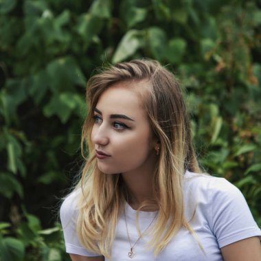 Yeşil bitki örtüsü bir arka plan üzerinde mesafe içine beyaz bir bluz sevimli sevimli sarışın görünüyor