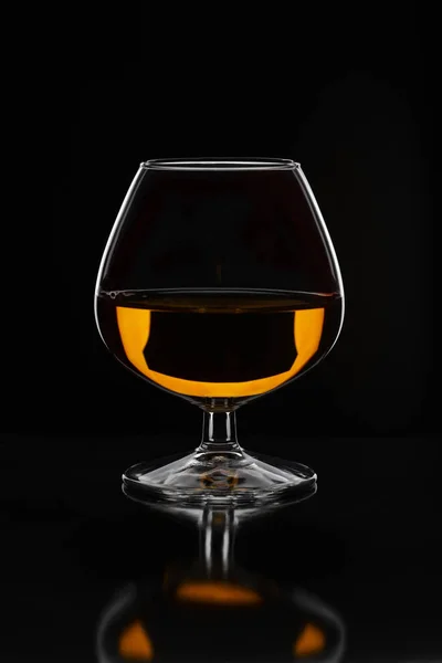 Brandy glass filled with half alcoholic drink on a black backgro — Stock Photo, Image