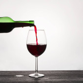 Červené víno se nalévá ze skleněné zelené láhve do sklenice na w