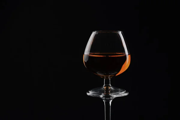 Ποτήρι μπράντι γεμάτο με μισό αλκοολικό ποτό σε μια μαύρη πλάτη — Φωτογραφία Αρχείου