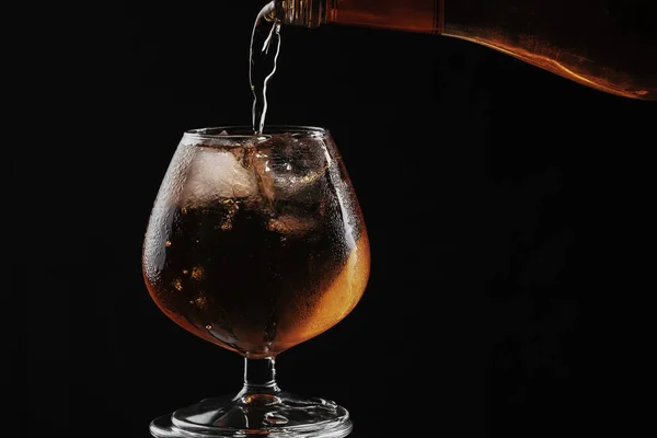 Whiskey is poured into a brandy glass with ice, the glass is ful — Stock Photo, Image