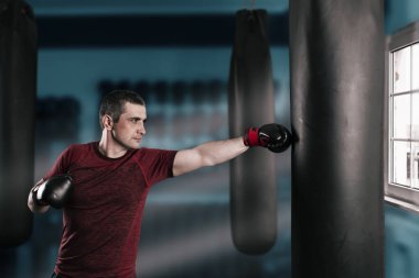 Genç kısa saçlı adam spor salonunda kum torbasıyla antrenman yapıyor..