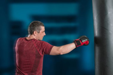 Genç kısa saçlı adam spor salonunda kum torbasıyla antrenman yapıyor..