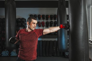 Genç kısa saçlı adam spor salonunda kum torbasıyla antrenman yapıyor..