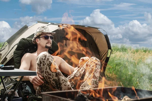 Hombre se sienta en una tienda de campaña turística en un día de verano en la naturaleza, en el fo — Foto de Stock