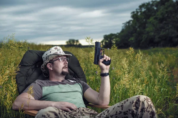 Mann mit Brille und Pistole in der Hand sitzt in einer Sitzecke — Stockfoto
