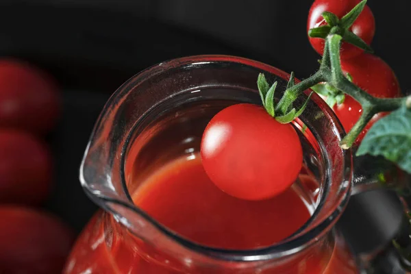 Cherry tomato hangs over the neck of a glass jug with tomato jui