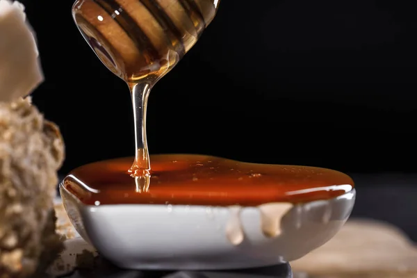 fresh honey flows from a wooden spoon into a small white outlet