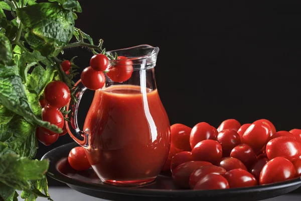 glass jug with tomato juice stands covered with cherry tomatoes