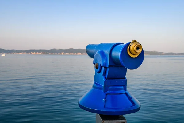 Blue public coin operated telescope, sea and island in background