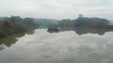 Uçan bir ormandaki bir erken sonbahar sabahı açık yansıtıcı bir göl yüzeyi yukarıda