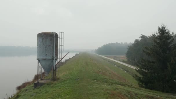 Lac brumeux réfléchissant tôt le matin d'automne avec un grand silo métallique, aérien — Video